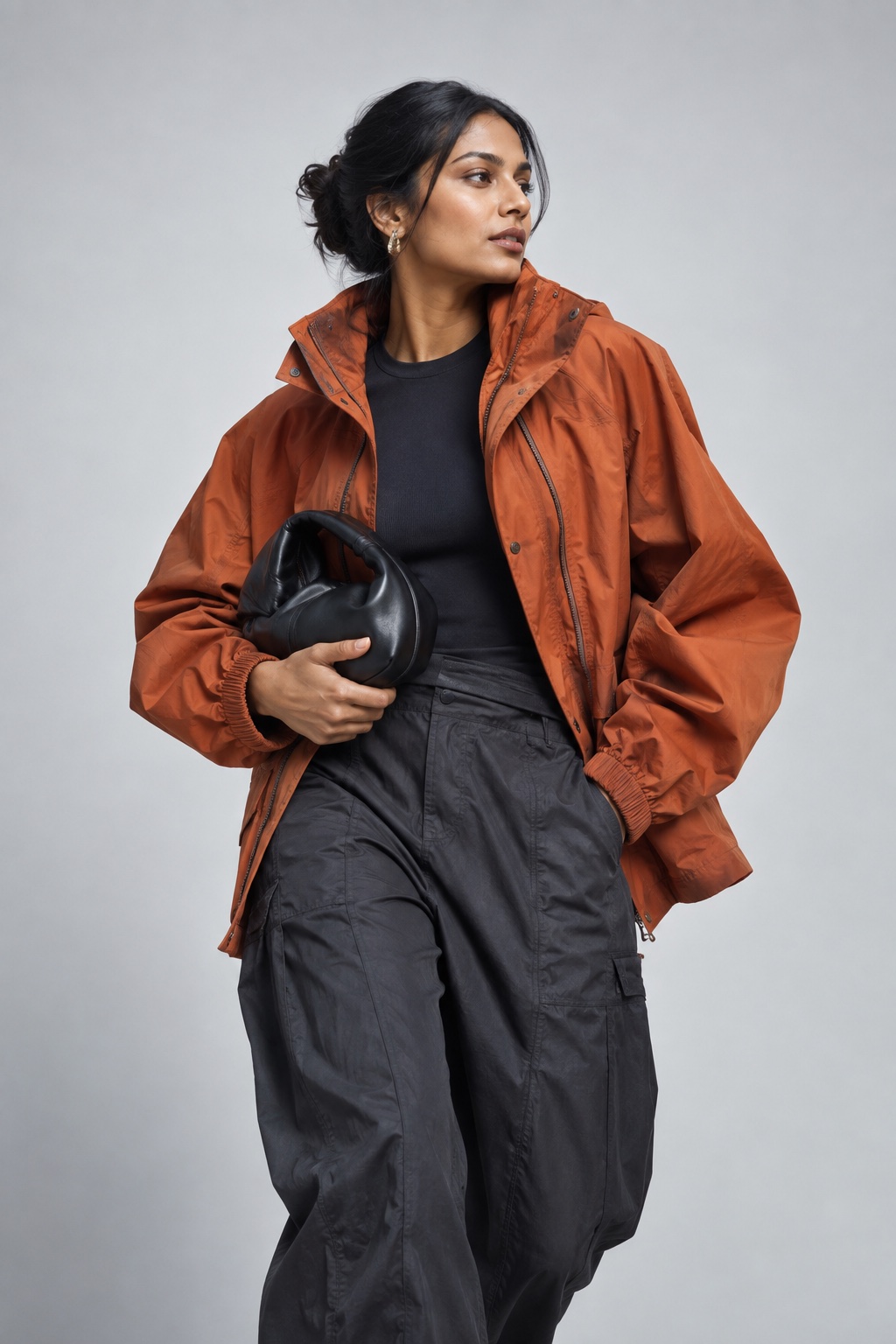 Original fashion study: a model wearing a rust-orange jacket against a cool grey backdrop